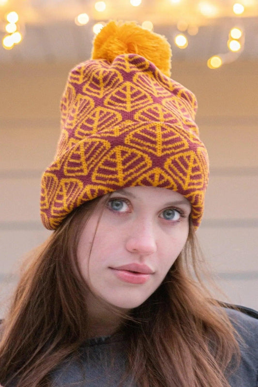 Model wearing the burgundy and gold leaf beanie under string lights