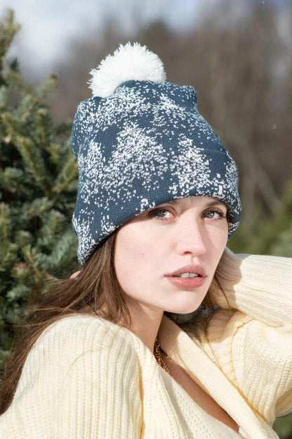 Model in the spruce pattern pom pom beanie, standing among evergreen trees