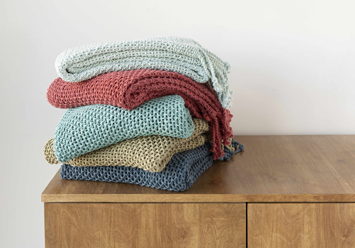 Stack of five folded knit throws in pale blue, red, aqua, tan and navy on a wooden cabinet