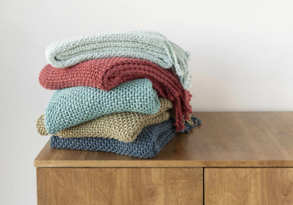 Stack of five folded knit throws in pale blue, red, aqua, tan and navy on a wooden cabinet