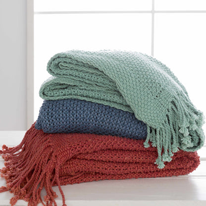 Aqua green knit throw folded on top of blue and red knit throws in front of a window