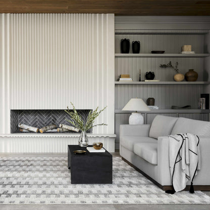 Cream knit throw blanket with a black grid draped over a light gray sofa in a living room with a fireplace