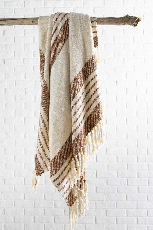 Cream and rust striped throw blanket hung over a wooden branch against a white brick wall, fringe at the bottom
