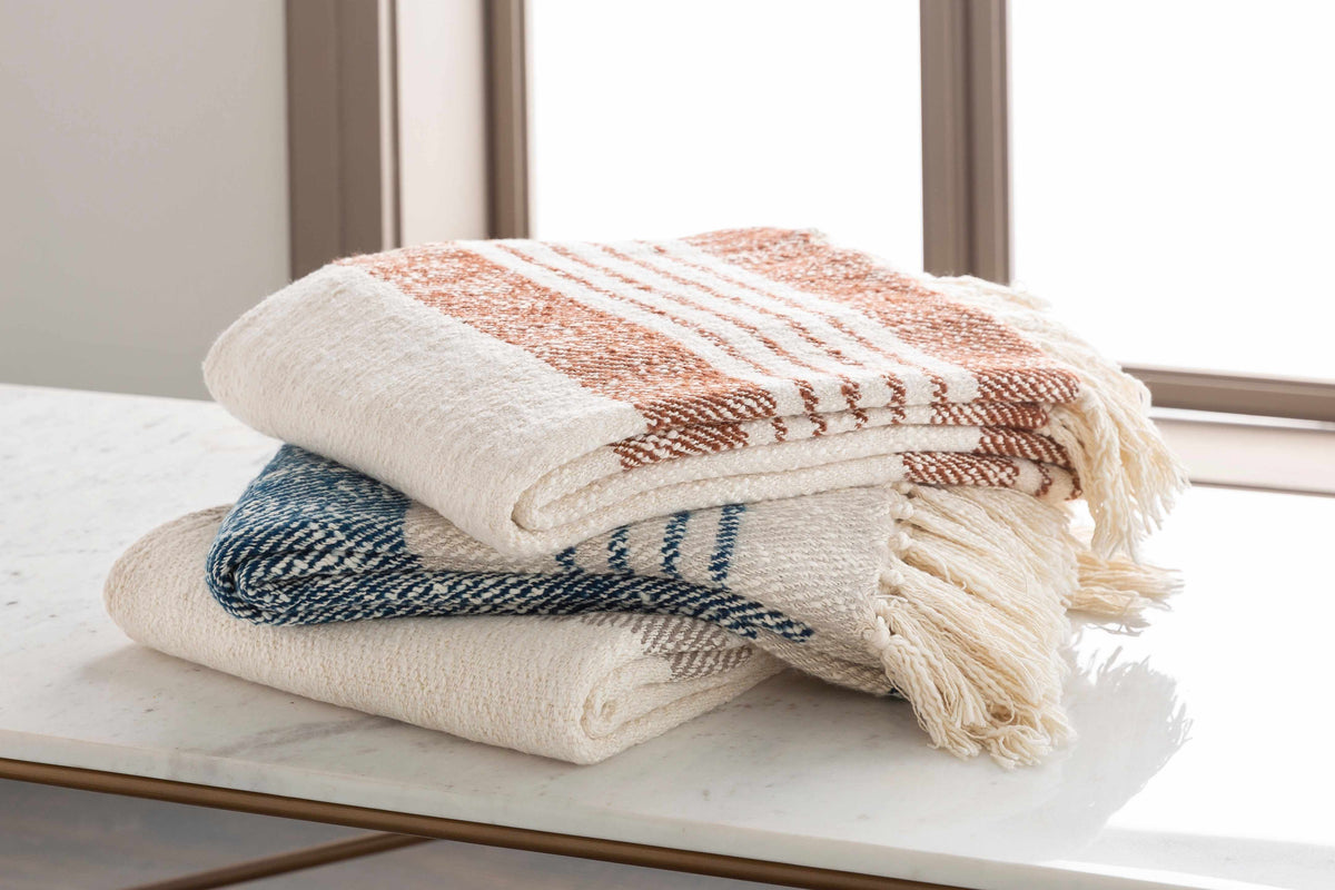 Folded cream and rust striped throw on top of two other woven throws on a white table by a window