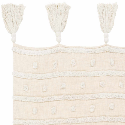 Close-up of the cream throw blanket showing tufted dots, raised stripes and three tassels with knotted tops
