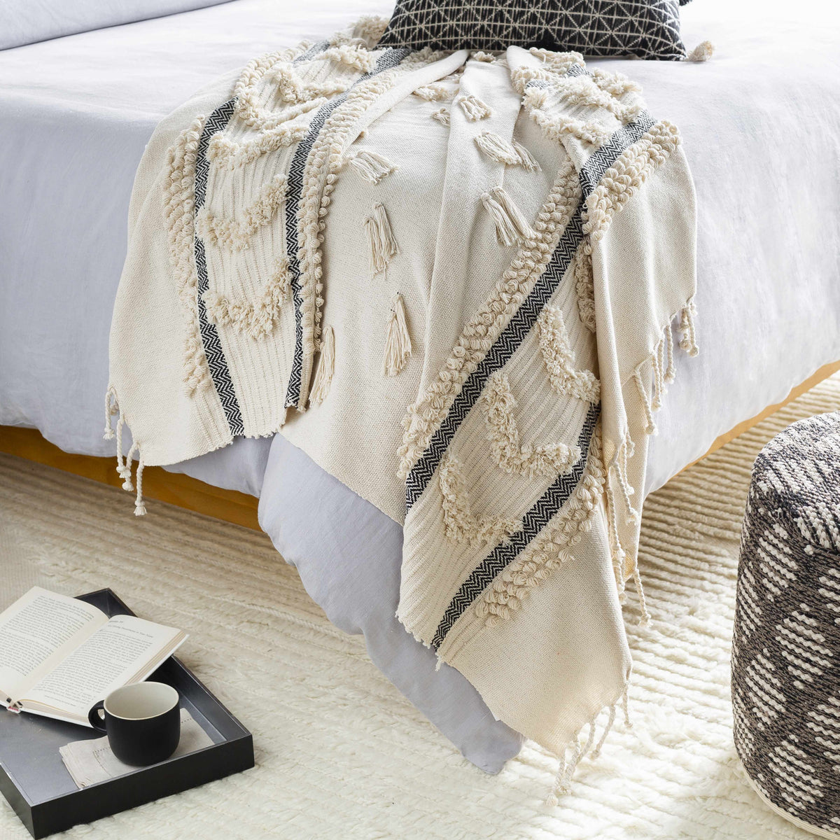 Ivory tufted throw blanket draped over the end of a bed, dark herringbone stripes and fringe reaching the floor