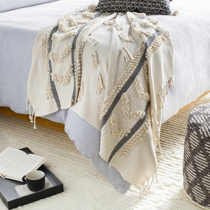 Ivory tufted throw blanket draped over the end of a bed, dark herringbone stripes and fringe reaching the floor