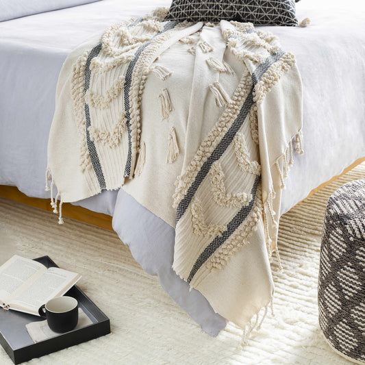 Ivory tufted throw blanket draped over the end of a bed, dark herringbone stripes and fringe reaching the floor