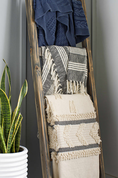 Ivory tufted throw blanket hanging on a wooden blanket ladder below two other throws, beside a potted snake plant