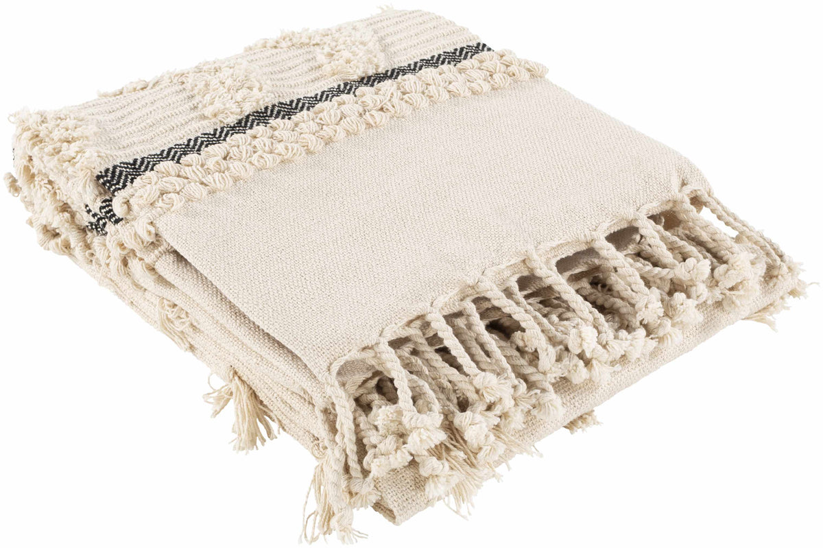Folded ivory cotton throw blanket seen at an angle, with chunky knotted fringe along one end