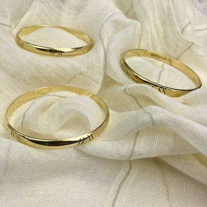 Three carved brass bangles laid on draped cream linen, their notches catching the light