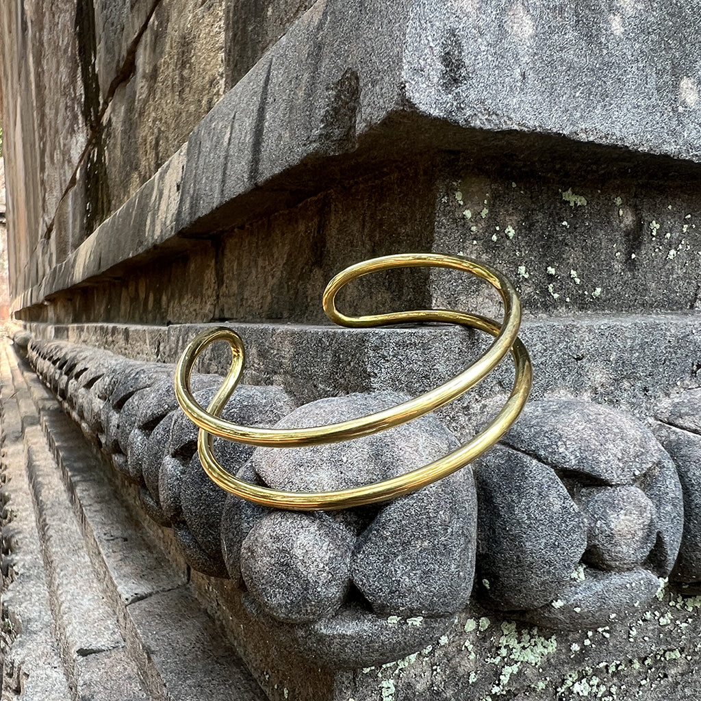 Double wire brass cuff resting on carved gray stone at the base of an old temple wall