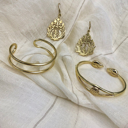 Brass wire cuff and lotus cuff on cream linen beside a pair of brass flame earrings