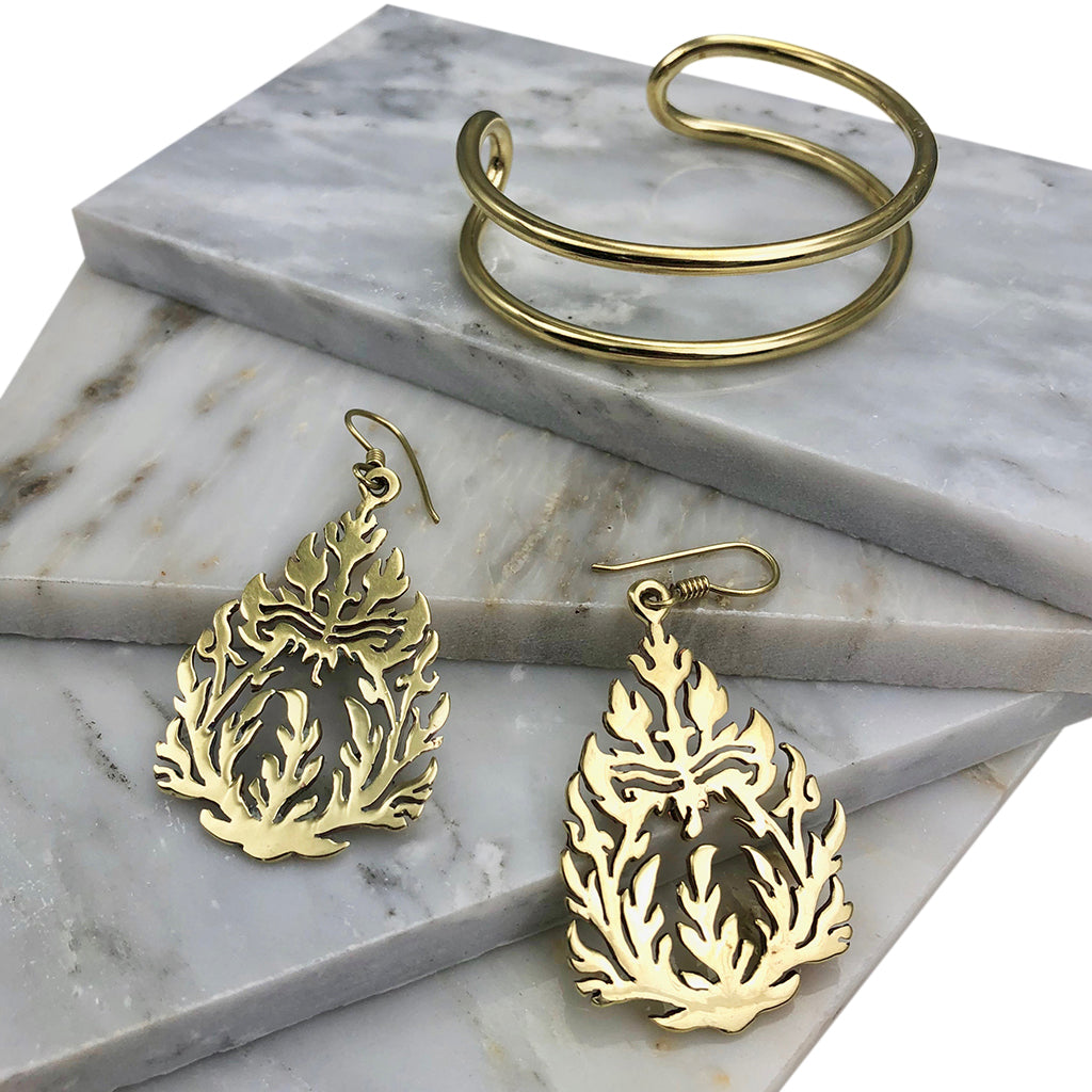 Double wire brass cuff on white marble tiles beside cutout brass flame earrings