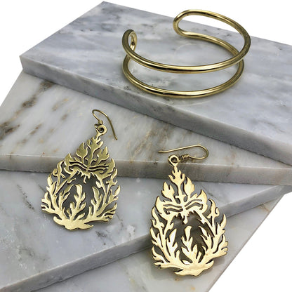 Double wire brass cuff on white marble tiles beside cutout brass flame earrings