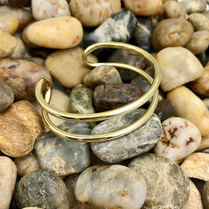 Double wire brass cuff bracelet resting on smooth river pebbles in brown and gray