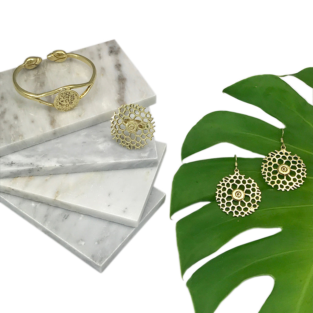 Brass lotus cuff on stacked marble with round cutout brass earrings beside a monstera leaf