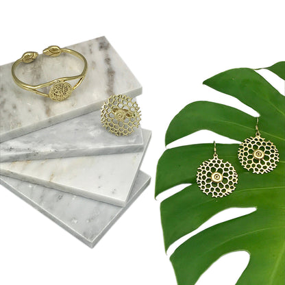 Brass lotus cuff on stacked marble with round cutout brass earrings beside a monstera leaf