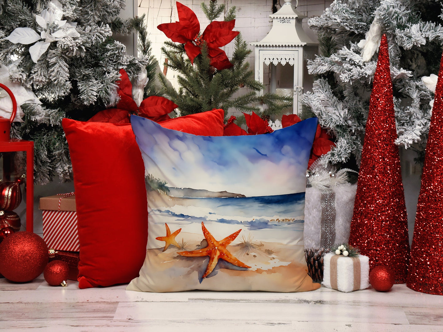 The Two starfish artwork pillow in a winter setting, among red cushions, poinsettia and frosted greenery.