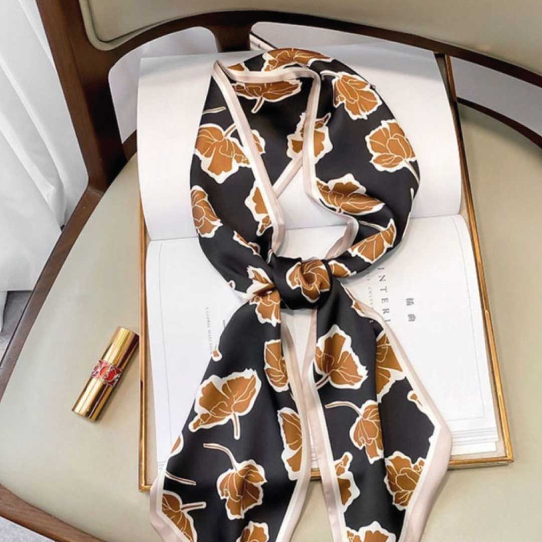 Brown Flowers colorway, a long silk scarf with caramel blooms on black and a cream edge, knotted on a book