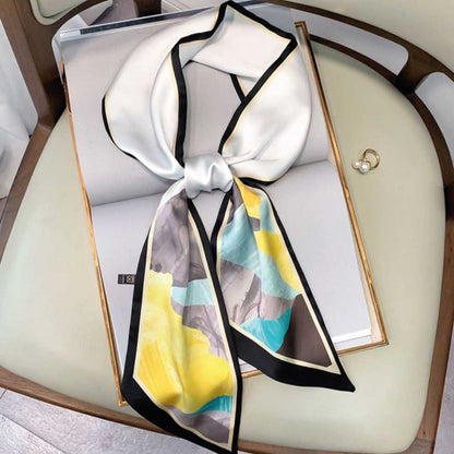 Skinny silk scarf knotted on a chair, white with yellow, turquoise and gray mountains and a black edge