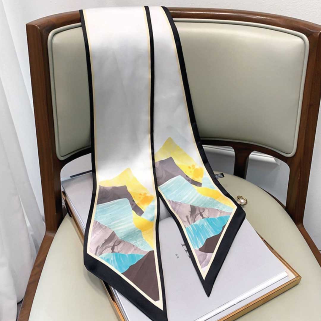 The black-edged skinny silk scarf hanging straight, its mountain print running down both ends