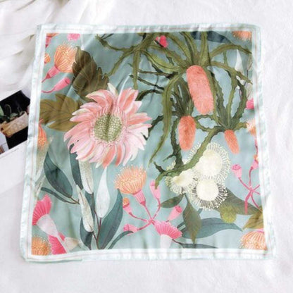 Square silk scarf in the green colorway laid flat, pink and peach flowers on soft sage with a pale edge