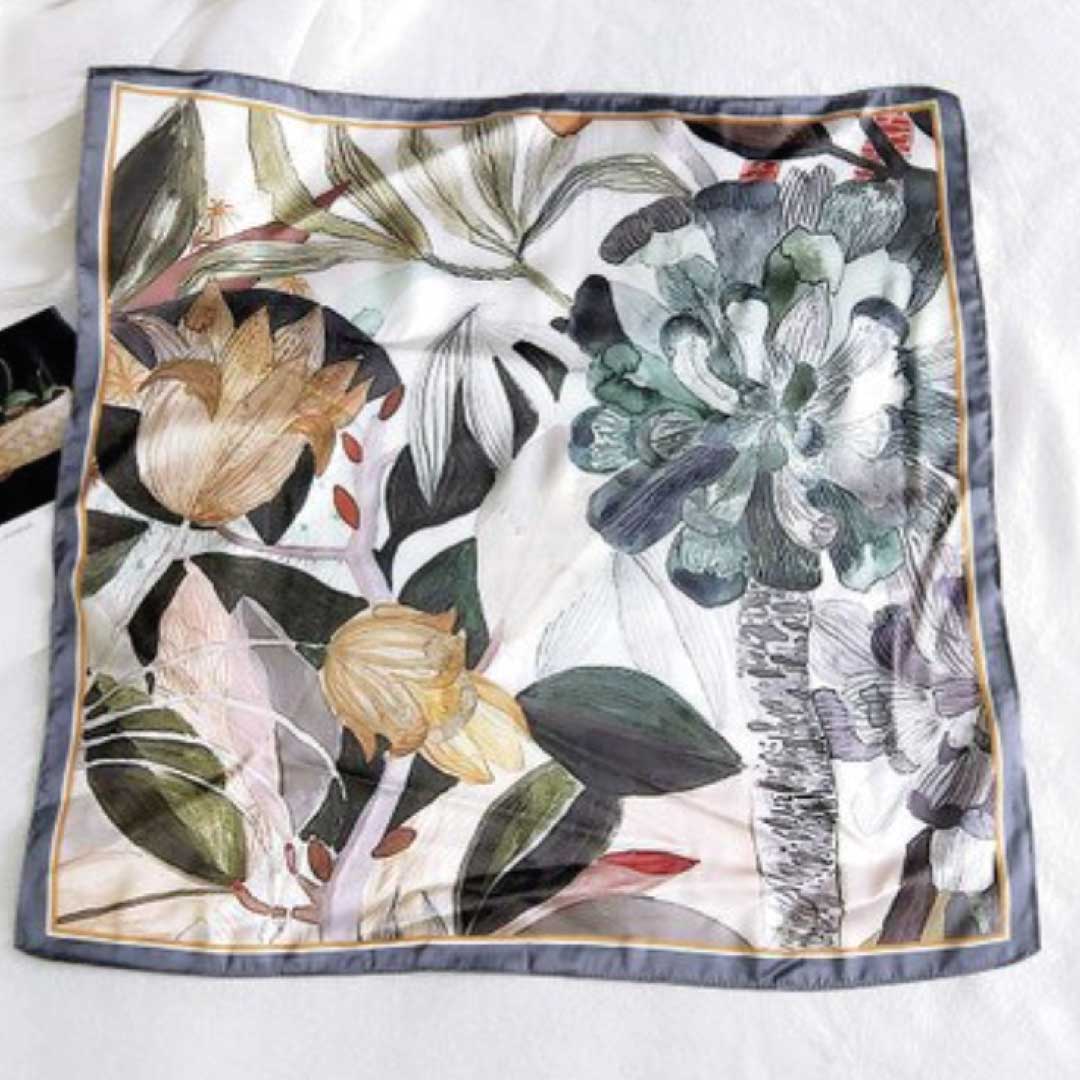 Square silk scarf in the gray colorway laid flat, gray and ochre botanicals on white inside a slate border