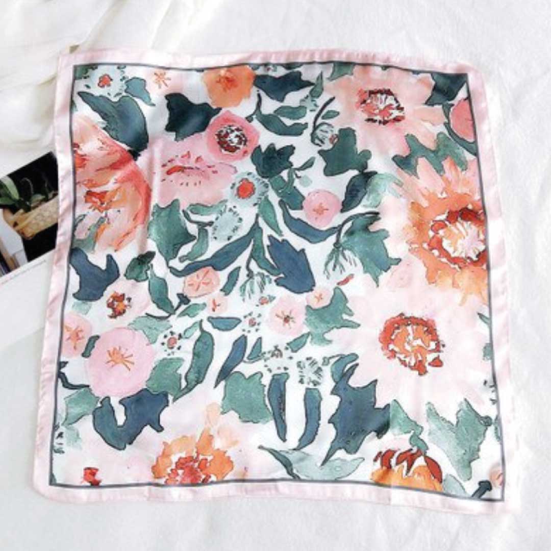 Square silk scarf in the rose colorway laid flat, coral and teal flowers on cream with a pink border