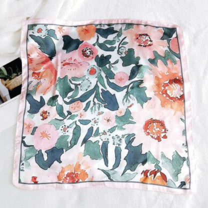 Square silk scarf in the rose colorway laid flat, coral and teal flowers on cream with a pink border