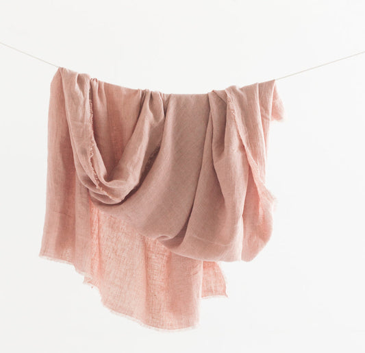 Blush pink stonewashed linen throw blanket hanging over a line, showing its soft rumpled drape and frayed edges