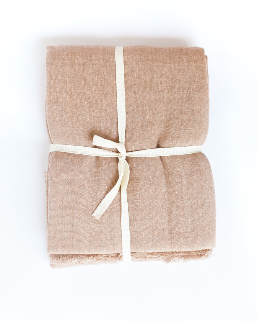 Folded blush linen throw blanket tied with a cream ribbon