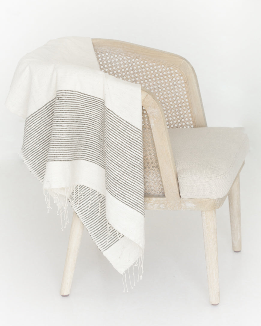 Natural cotton throw with a wide band of fine gray stripes draped over a cane back wooden chair
