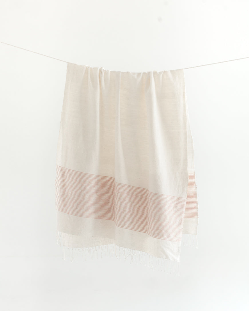 Natural cotton throw with a band of blush pink stripes hanging from a line, fringe at the bottom