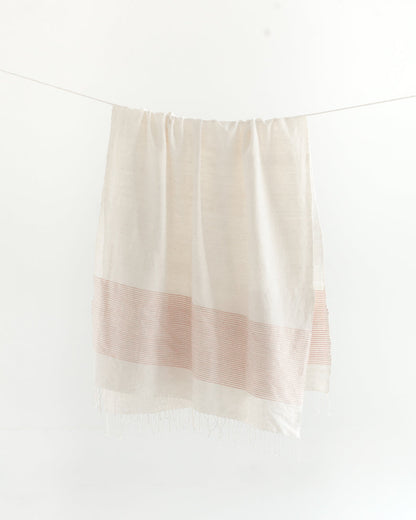 Natural cotton throw with a band of blush pink stripes hanging from a line, fringe at the bottom