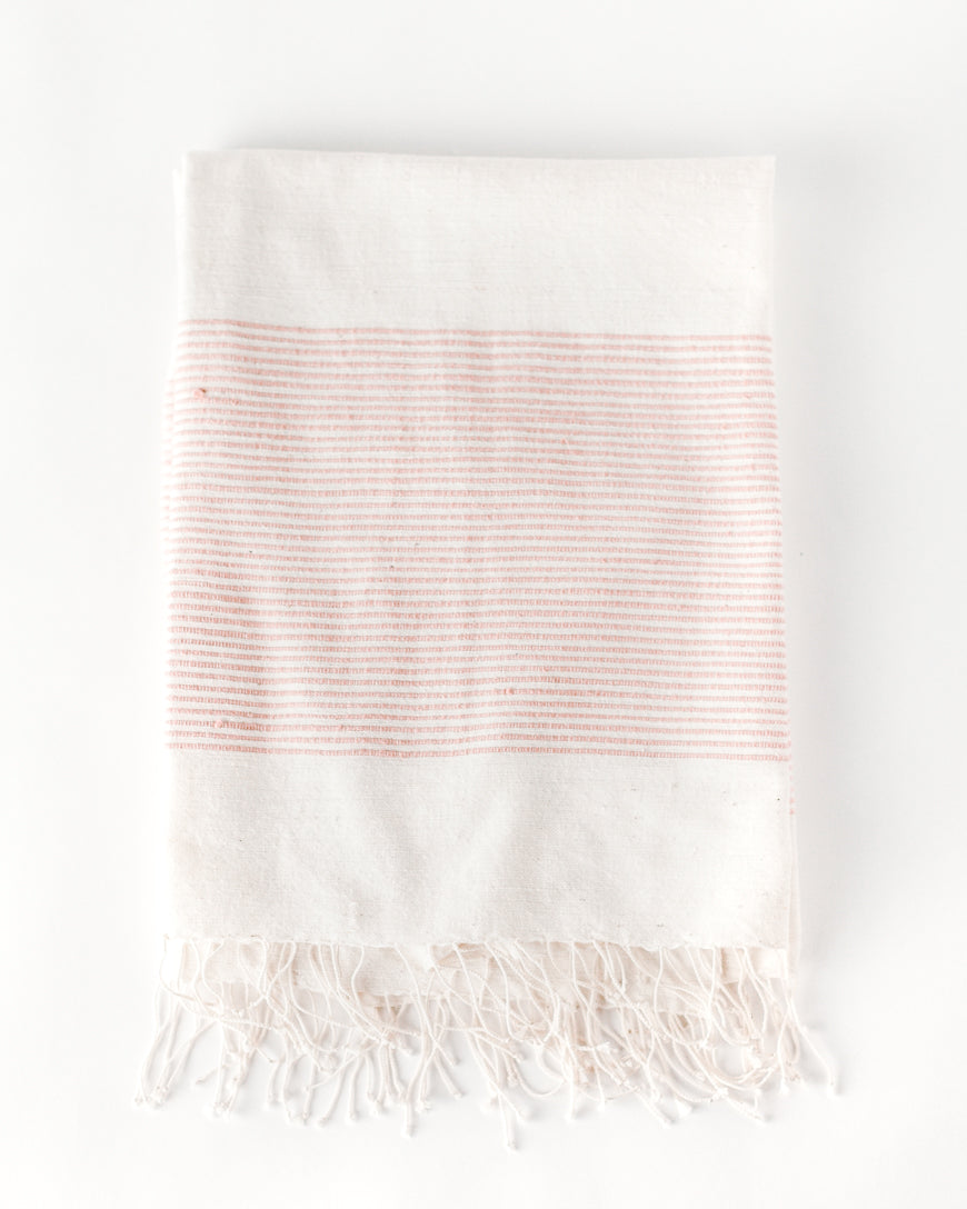 Flat view of the natural cotton throw with a wide band of fine blush stripes and knotted fringe