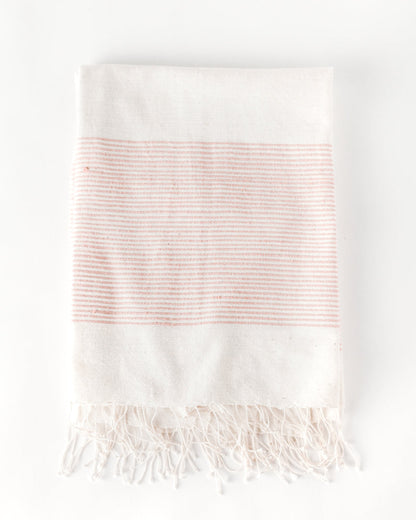Flat view of the natural cotton throw with a wide band of fine blush stripes and knotted fringe