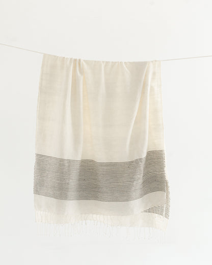 Natural cotton throw with a band of gray stripes hanging from a line, knotted fringe at the hem