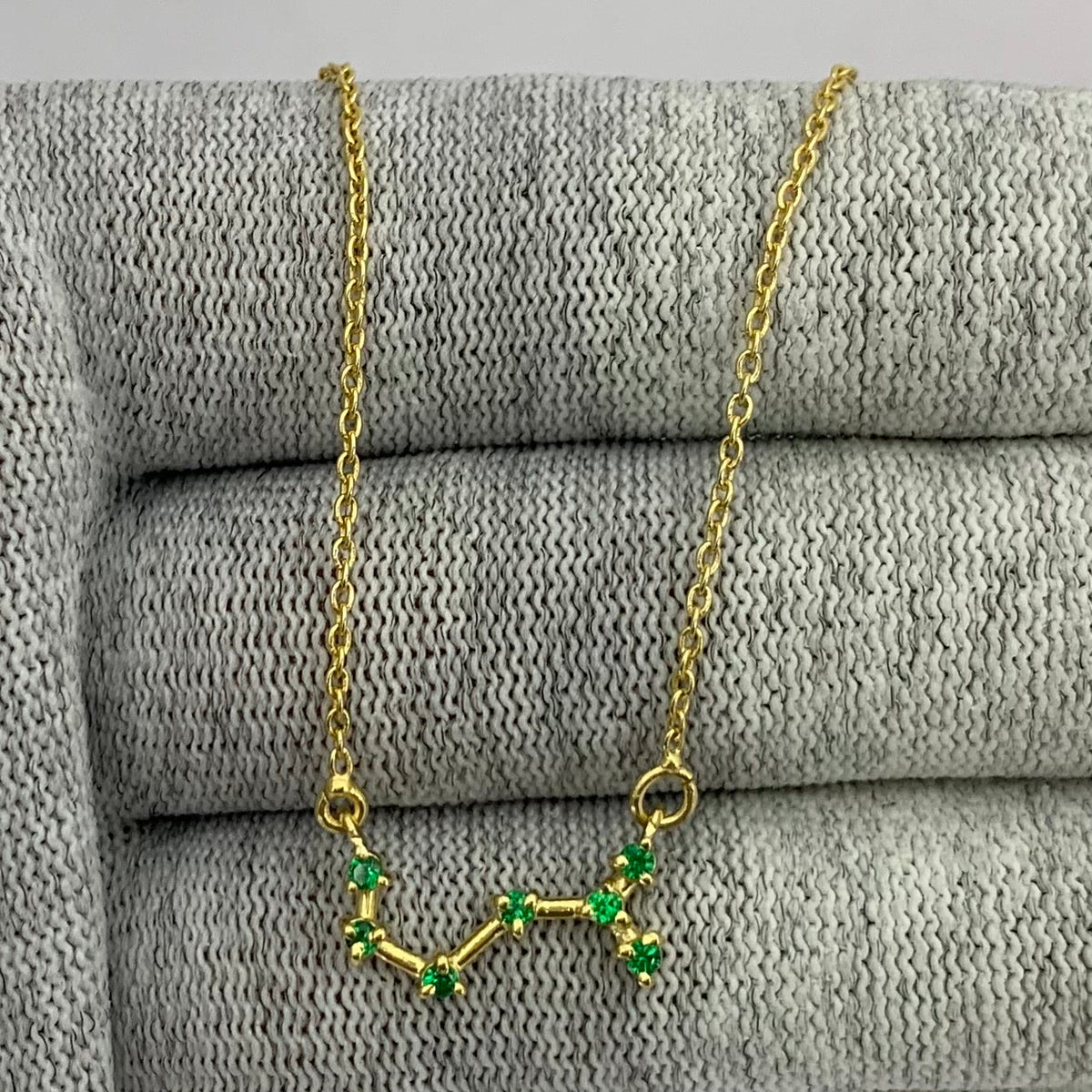 Constellation necklace with seven green tourmaline stones linked by gold tone bars over gray knit