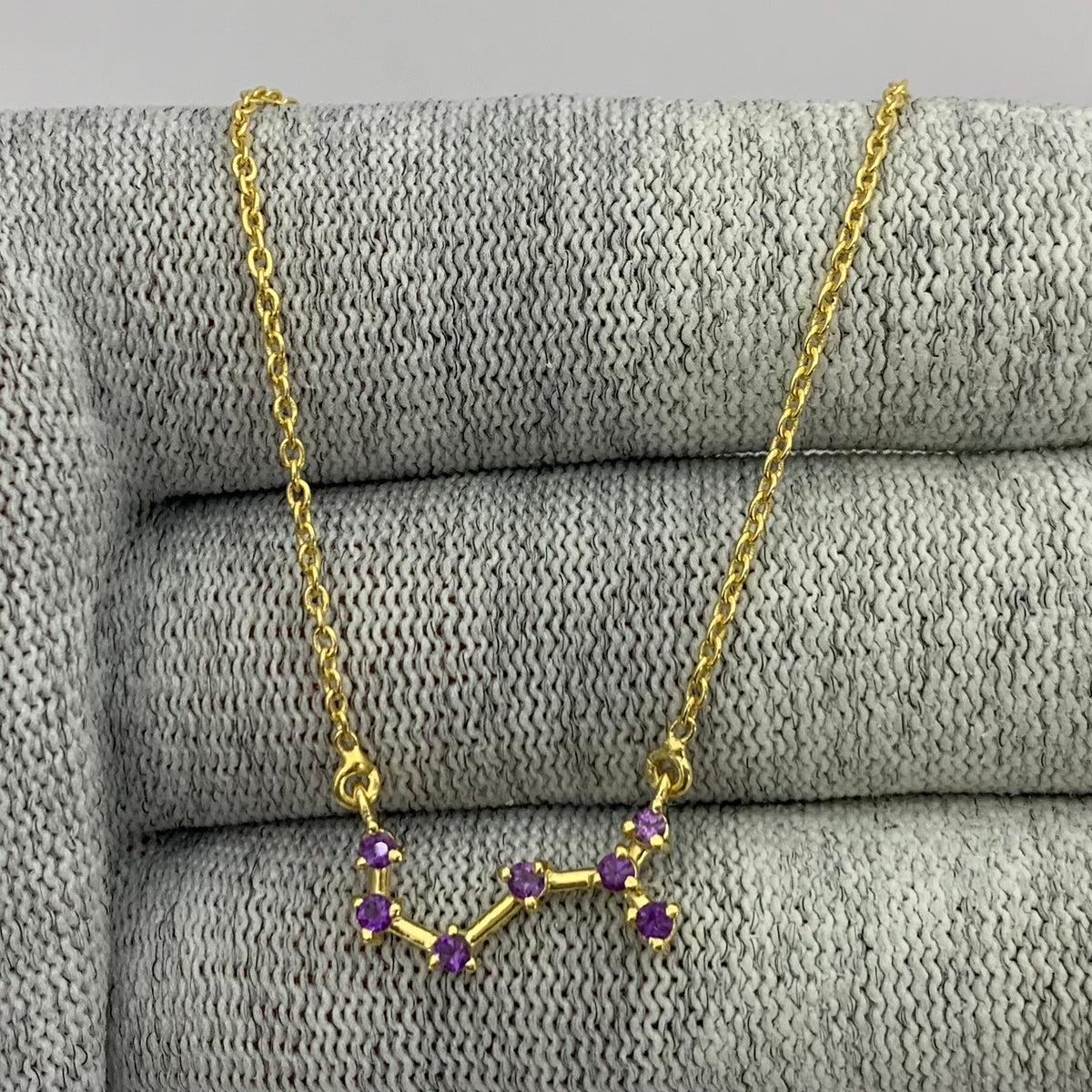 Constellation necklace with seven purple amethyst stones draped over gray knit fabric