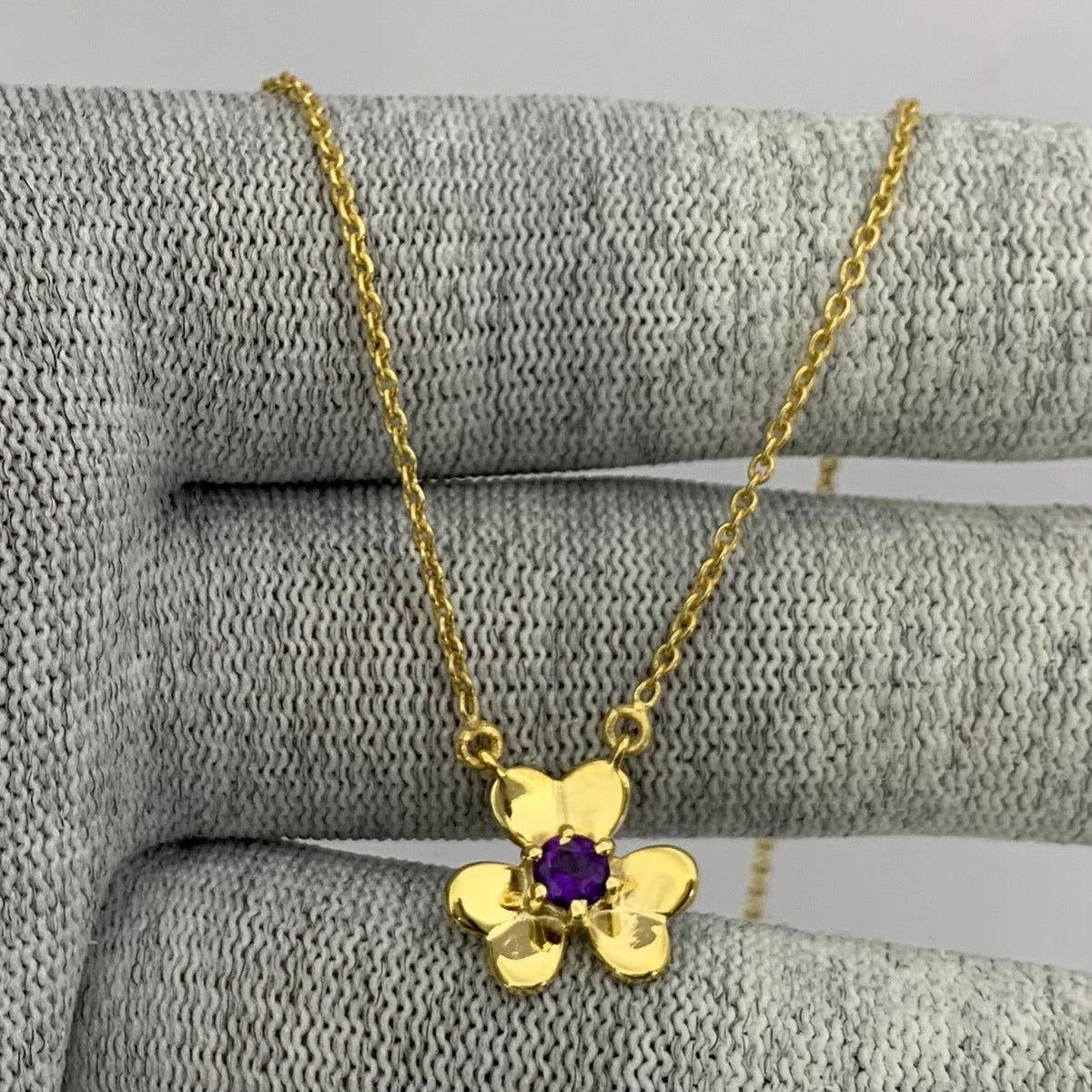 Three petal gold tone flower with a purple amethyst center, chain draped over gray knit