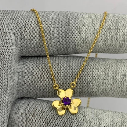 Three petal gold tone flower with a purple amethyst center, chain draped over gray knit