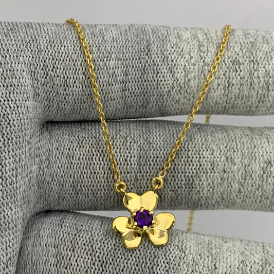 Three petal gold tone flower with a purple amethyst center, chain draped over gray knit