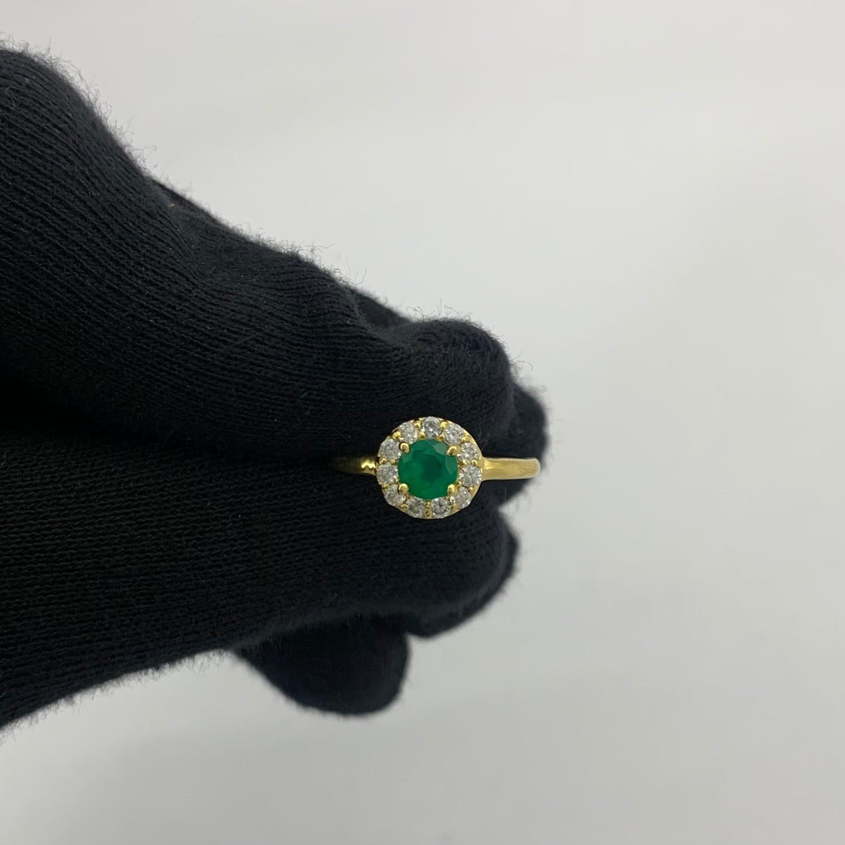Green onyx halo ring held between two gloved fingertips to show its size
