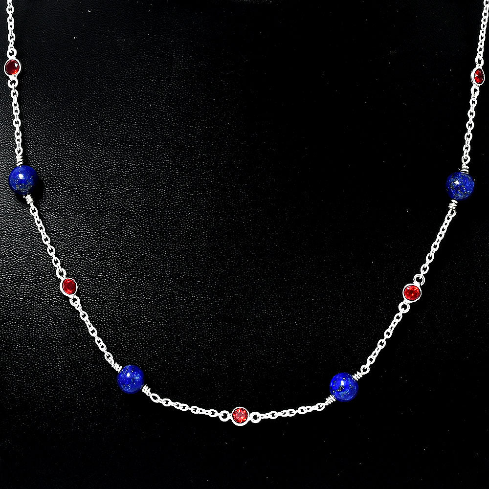 Close view of round blue lapis beads and bezel set red garnets on a silver chain against black