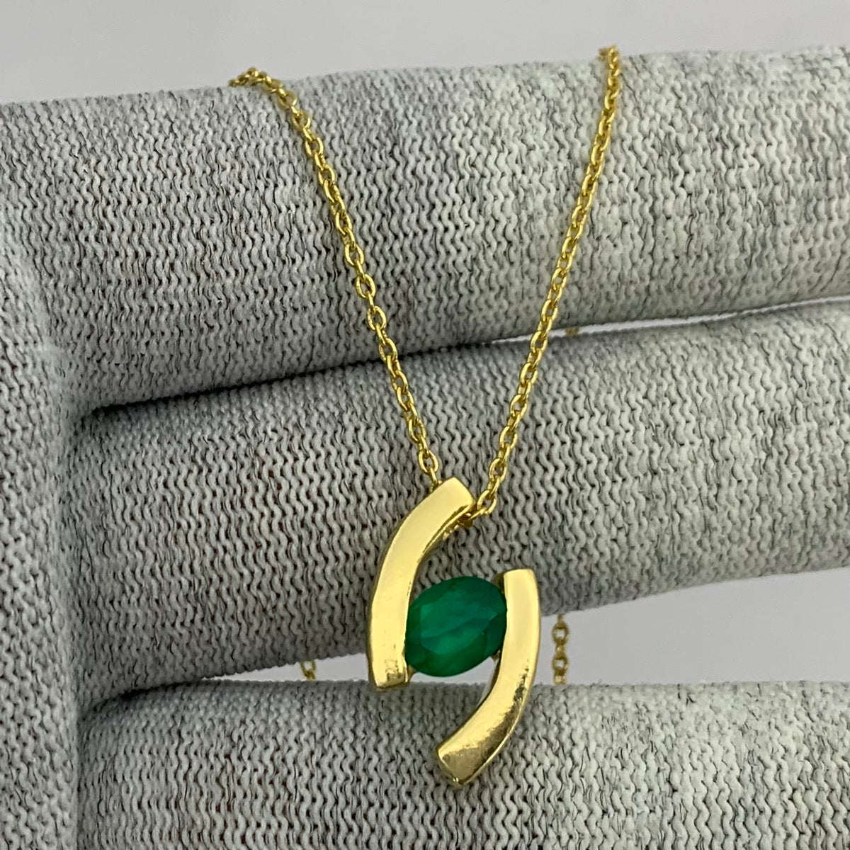 Oval green onyx held between two curved gold tone bars, pendant draped over gray knit