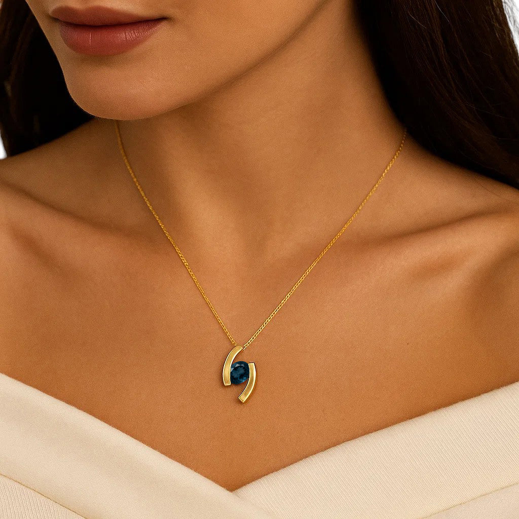 Woman in a cream off shoulder top wearing the pendant with a dark blue London blue topaz