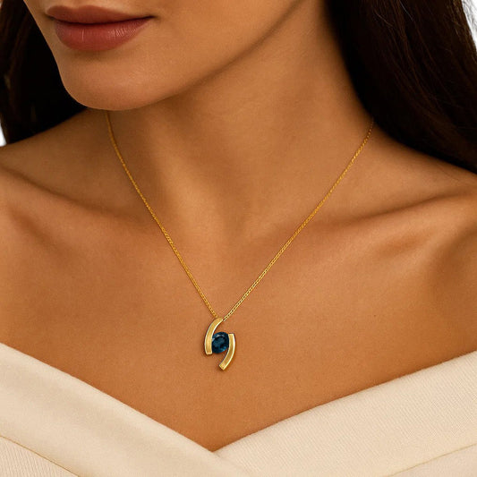 Woman in a cream off shoulder top wearing the pendant with a dark blue London blue topaz