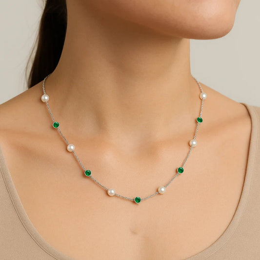 Woman in a beige top wearing the pearl station necklace with green onyx stones along the neckline
