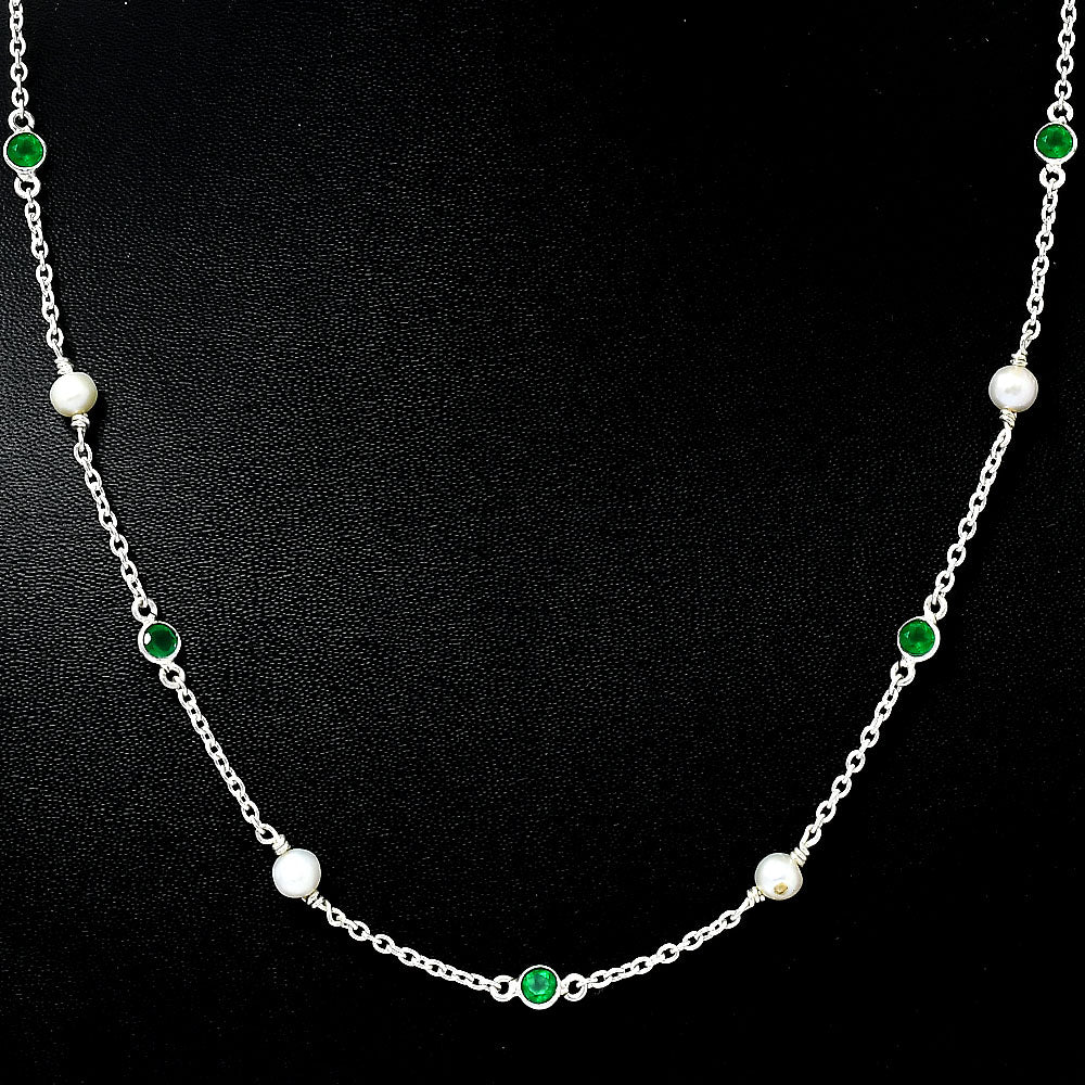 Close view of white pearls and bezel set green onyx stones on a silver chain against black
